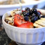 picture of a smoothie with granola, blueberries, strawberries, and bananas in a white bowl on a counter from "Acai Smoothie Bowl" by Green Smoothie Girl