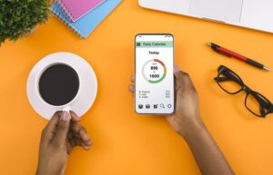 Woman's hands holding phone with calorie counting app and a cup of coffee from "6 Reasons I Hate Calorie Counting And Don't Do It" by Green Smoothie Girl