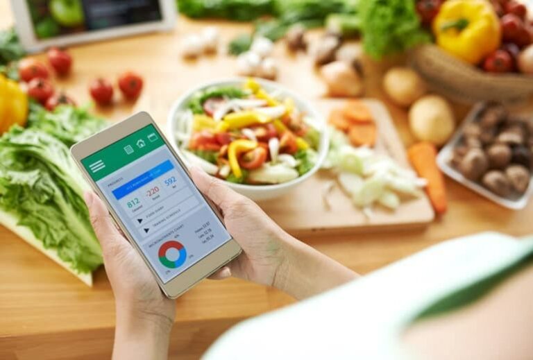 Photo of hands holding calorie counting app on phone with food in background from "Six Reasons I Hate Calorie Counting and Don't Do It" by Green Smoothie Girl