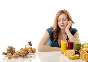 Photo of woman sitting at table in front of healthy foods, looking longingly at pile of pastries from "{VIDEO} Why Are You Afraid of Detoxing?" by Green Smoothie Girl