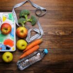 Photo of water bottle, apples, carrots, broccoli, scale, soft measuring tape on wooden background from "{VIDEO} How to Change Your Weight “Set Point” Forever" by Green Smoothie Girl