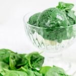 several scoops of green ice cream in a clear bowl next to a bile of spinach from Green Smoothie Girl's "Green Ice Cream"