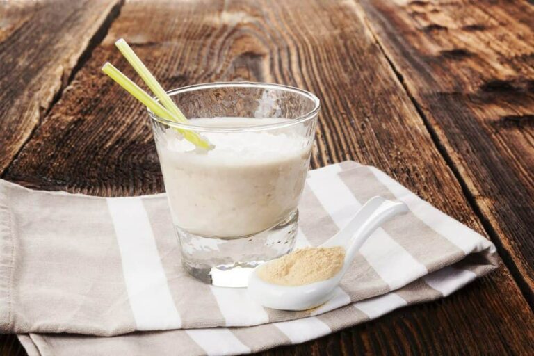 Photo of clear glass with white protein drink and scoop of bone broth protein on striped towel from "Bone Broth Protein: Why You Should Try It" by Green Smoothie Girl