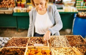 Photo of a woman choosing almonds in a grocery store nut display from "13 Top Raw Almonds Nutrition Benefits (And How To Get Truly Raw Almonds)" by Green Smoothie Girl