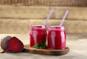 Photo of two pink smoothies in glass jar with striped straws and cut beet on the side from "Hot Pink Smoothie" recipe by Green Smoothie Girl