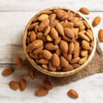 Photo of bowl of almonds on wooden table from "13 Top Raw Almonds Nutrition Benefits (And How To Get Truly Raw Almonds)" by Green Smoothie Girl
