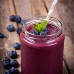 Photo of purple smoothie in tall glass with mint blueberries and striped straw from "Blueberry Mango Smoothie" recipe by Green Smoothie Girl