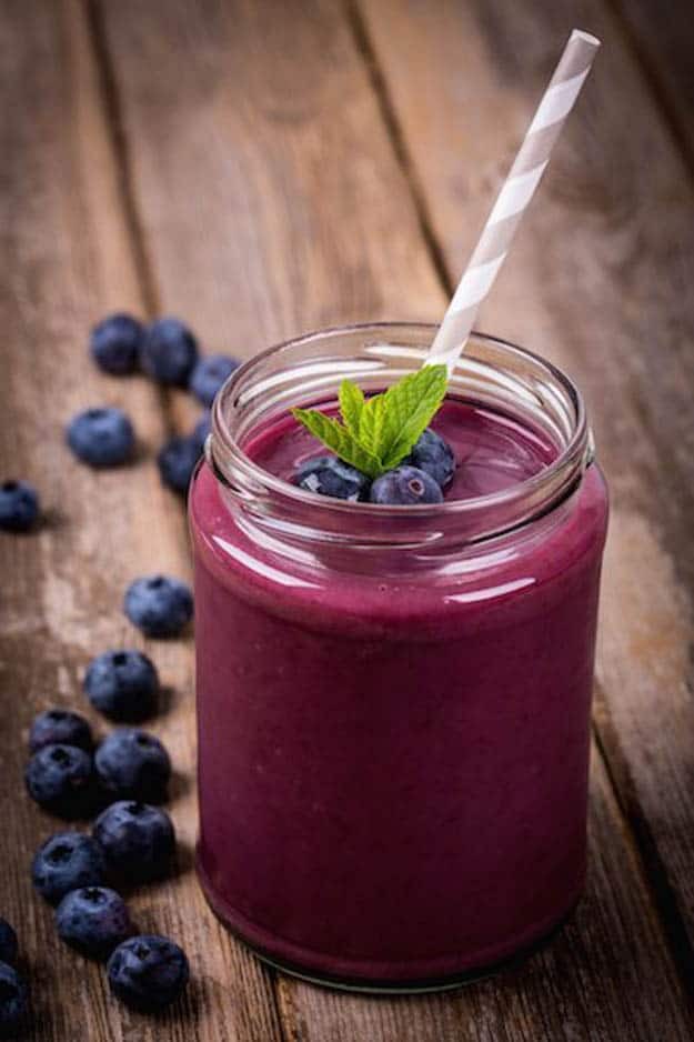 Photo of purple smoothie in tall glass with mint blueberries and striped straw from "Blueberry Mango Smoothie" recipe by Green Smoothie Girl