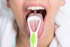 Close-up photograph of a person using a tongue scraper. From "How to Use a Tongue Scraper (and Why You Should Make it a Habit)" at Green Smoothie Girl.
