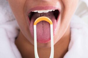 Close-up photograph of a person using a tongue scraper. From "How to Use a Tongue Scraper (and Why You Should Make it a Habit)" at Green Smoothie Girl.
