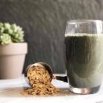 Photo of green smoothie in glass with measuring cup spilling out oats with plant in background from "Oatmeal Breakfast Smoothie" recipe by Green Smoothie Girl