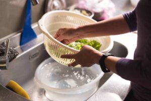 Photograph of a person washing vegetables in a kitchen sink, from "How To Freeze Spinach and Other Leafy Greens For Later (With Shortcuts!)" at Green Smoothie Girl.