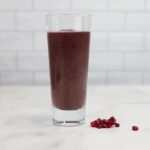 Photograph of a purple Tart Berry Blast Green Smoothie with pomegranate seeds next to it from "10 Easy Green Smoothies Kids Will Love" recipe by Green Smoothie Girl