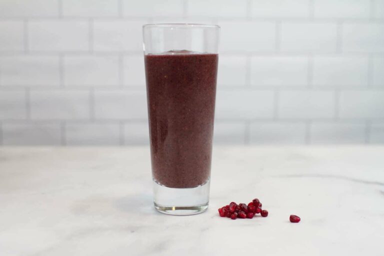 Photograph of a purple Tart Berry Blast Green Smoothie with pomegranate seeds next to it from "10 Easy Green Smoothies Kids Will Love" recipe by Green Smoothie Girl