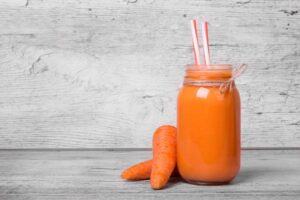 Photograph of a smoothie next to two raw carrots, from "Healthiest Smoothie Recipes for Each Season of the Year" at Green Smoothie Girl.