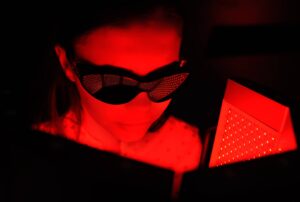 Photograph of a young woman receiving red light therapy and wearing protective goggles, from "The Health Benefits of Red Light Therapy: Legit or Hype?"