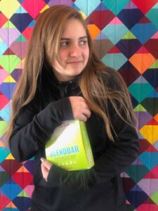 Photograph of a teenage girl holding a box of Blendbars against a multi-colored background, from "Why Most Nutrition Bars are Garbage -- and What to Pack in Your Purse Instead" at Green Smoothie Girl