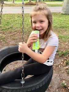 Photograph of a young girl on a tire swing eating a Blendbar nutrition bar, from "Why Most Nutrition Bars are Garbage -- and What to Pack in Your Purse Instead" at Green Smoothie Girl