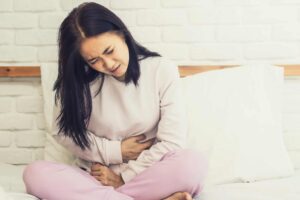 Woman sitting in bed with abdominal pain, from "Natural Treatments for Urinary Tract Infections (UTIs)" at Green Smoothie Girl.