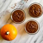 three brown smoothies next to a pumpkin from Green Smoothie Girl's "peanut butter pumpkin pick-me-up smoothie"