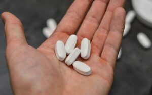 Photograph of a hand holding five white supplement pills, from "Vitamin C: Ascorbic Acid Supplements Can Hurt Your Health" at Green Smoothie Girl.