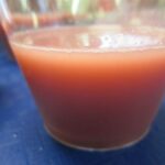 Photograph of a pink drink in a small transparent cup, sitting on a blue tablecloth.