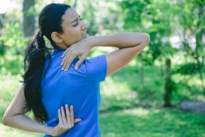 Photo of young woman in pigtail feeling pain from back soft tissue damage from "How (And Why) To Do Lymphatic Drainage Massage On Yourself" by Green Smoothie Girll