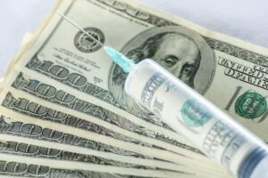 Photo of syringe and needle on top of hundred dollar bills from "Open Letter To A Cancer Patient: My Alternative Cancer Treatment Plan" by Green Smoothie Girl