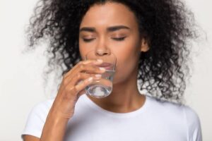 Photo of African American woman in white shirt drinking water from "How (And Why) To Do Lymphatic Drainage Massage On Yourself" by Green Smoothie Girl