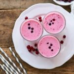 Photo of pink yogurt with cranberries in glasses on white plate with wooden background from "Cranapple Yogurt Crave" recipe by Green Smoothie Girl