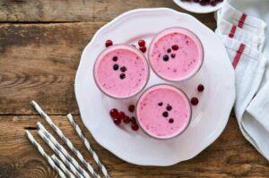 Photo of pink yogurt with cranberries in glasses on white plate with wooden background from "Cranapple Yogurt Crave" recipe by Green Smoothie Girl