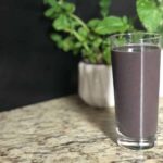 Photo of purple smoothie in tall glass with two plants in white pots behind it from "Morning Berry Smoothie" recipe by GreenSmoothieGirl