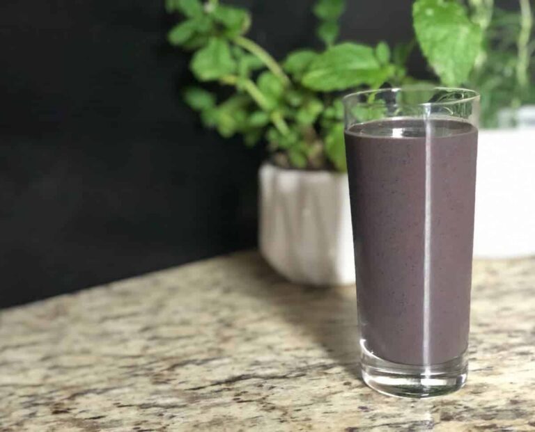 Photo of purple smoothie in tall glass with two plants in white pots behind it from "Morning Berry Smoothie" recipe by GreenSmoothieGirl