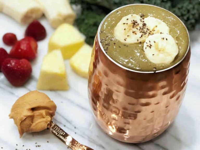 Photo of green smoothie in copper cup with kale, banana, strawberries, pineapple, banana, chia seeds, peanut butter surrounding from "Banana Split Smoothie" recipe by Green Smoothie Girl