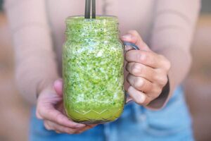 Photo of hands holding pinapple spinach green smoothie in mason jar from "Green Smoothies For Crohn’s Disease: Research And Recipes" by Green Smoothie Girl