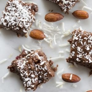 Photo of chocolate almond coconut fudge surrounded by coconut slivers and almonds from "Healthy Holiday Treats" by Green Smoothie Girl