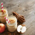 Photo of apple cinnamon smoothie with apples and cinnamon sticks in background from "Warm Apple Smoothie" recipe by Green Smoothie Girl