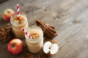 Photo of apple cinnamon smoothie with apples and cinnamon sticks in background from "Warm Apple Smoothie" recipe by Green Smoothie Girl