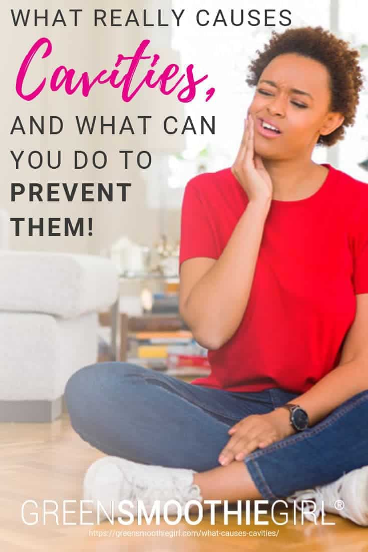 Photo of young black woman sitting on floor holding jaw in pain with post's text from "What Really Causes Cavities, and What Can You Do to Prevent Them?" by Green Smoothie Girl