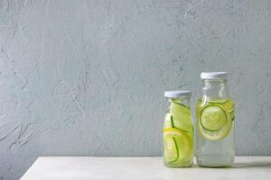 Photo of two clear glass bottles of water with lemon and cucumber slices in them from "What Can You Drink During Modified Fasting? Tips, Recipes, and Best Practices" by Green Smoothie Girl