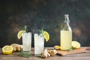 Photo of two cold glasses of ginger lemon water with bottle on table from "What Can You Drink During Modified Fasting? Tips, Recipes, and Best Practices" by Green Smoothie Girl