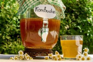 Photo of kombucha in a glass dispenser on an outside table from "What Can You Drink During Modified Fasting? Tips, Recipes, and Best Practices" by Green Smoothie Girl