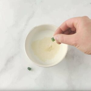 Photo of bowl of milk on marble counter with hand pouring open probiotic capsule contents in from "How to Test your Probiotic Supplement at Home"by Green Smoothie Girl