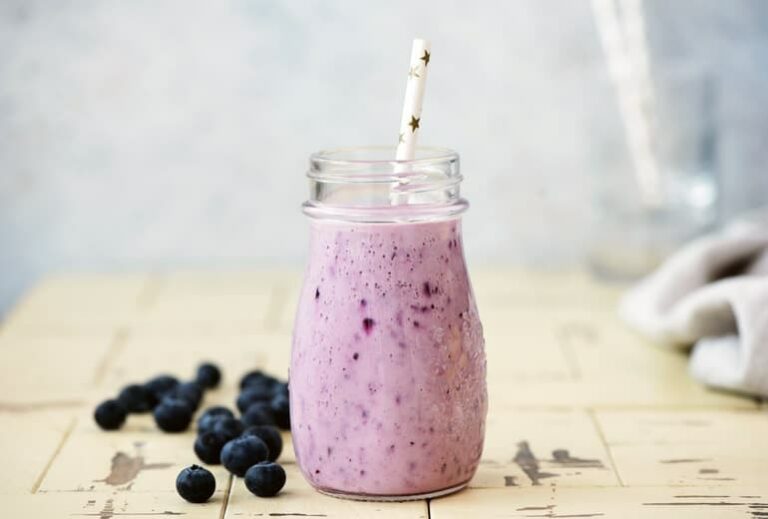 Photo of purple berry smoothie in glass jar with paper straw and blueberries surrounding from "3-Day Modified Fasting Eating Plan and Sample 3-Day Menu" by Green Smoothie Girl