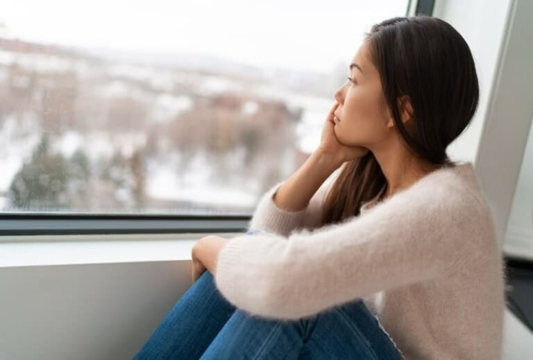 Photo of sad Asian woman looking out window from "10 Green Smoothies For Seasonal Affective Disorder" by Green Smoothie Girl