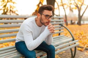 Photo of young man wearing glasses with sad expression sitting on park bench with yellow autumn leaves around from "10 Green Smoothies For Seasonal Affective Disorder" by Green Smoothie Girl