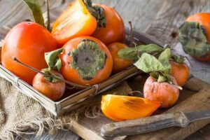 Photo of fresh whole and cut persimmons on wooden board with knife from "10 Green Smoothies For Seasonal Affective Disorder" by Green Smoothie Girl