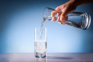 Photo of hand pouring clean water from glass pitcher to glass cup from "How To Cycle 3-Day Modified Fasts For Healthy, Sustainable Weight Loss" blog post by Green Smoothie Girl