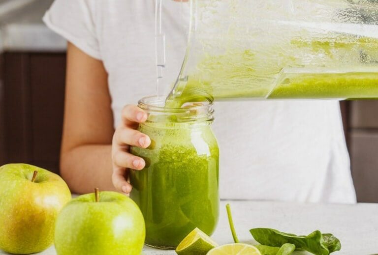 Photo of green smoothie being poured from blender into glass jar held by woman's hand from "11 Green Smoothie Recipes for Fatty Liver" by Green Smoothie Girl