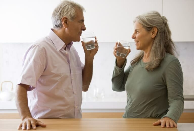 Photo of mature couple smiling at each other and drinking water in kitchen from "9 Tips For Sailing Through a 3-Day Modified Fast" blog post by Green Smoothie Girl